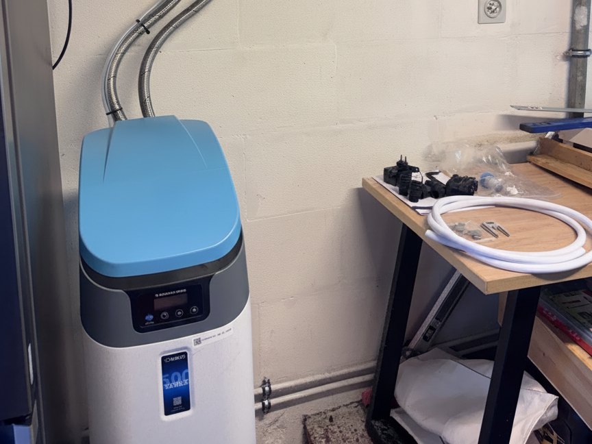 Adoucisseur au sel Valeco 500 Series posé contre le mur du local technique, relié par ses flexibles inox