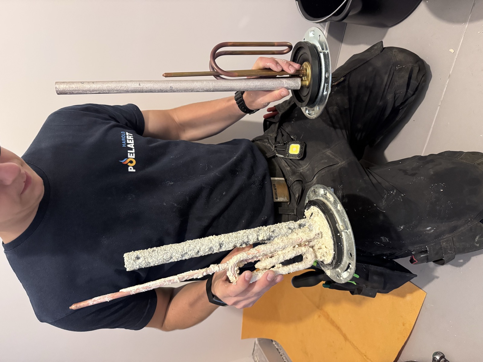 Comparaison de l'ancienne résistance entartrée et de la pièce neuve tenues par le technicien