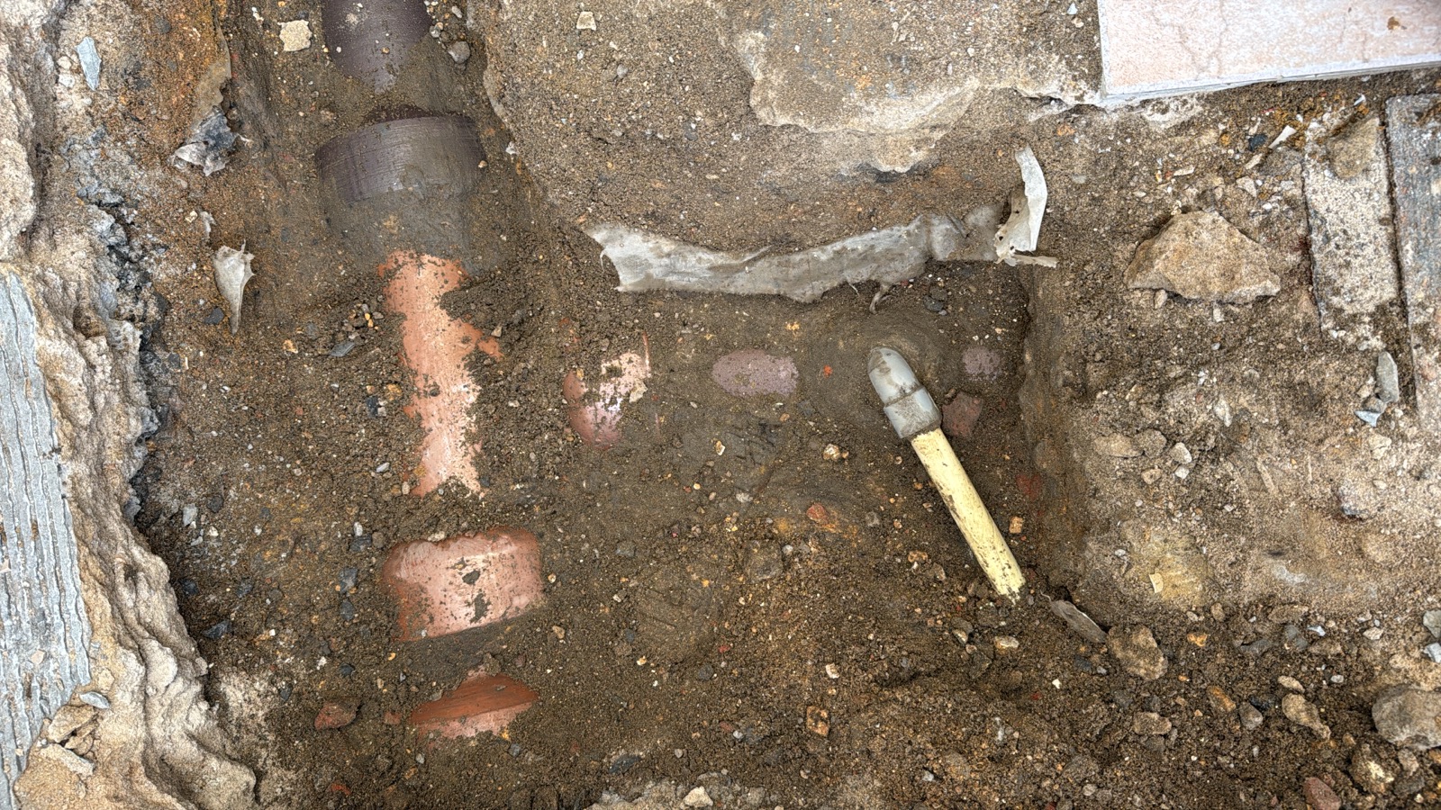 Sol carrelé ouvert, tranchée creusée laissant apparaître l'ancienne canalisation enterrée en grès